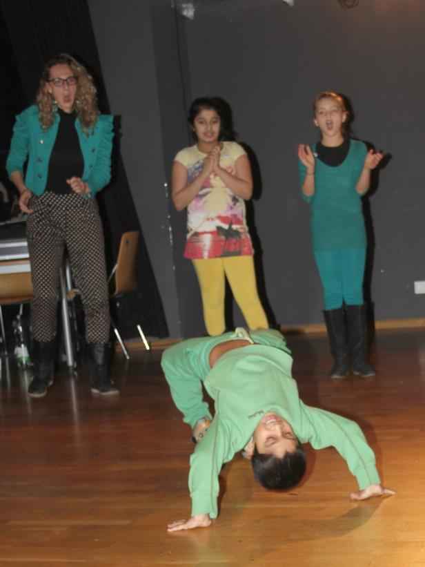 Ein Junge macht einen Handstand, während drei Mädchen im Hintergrund zusehen.