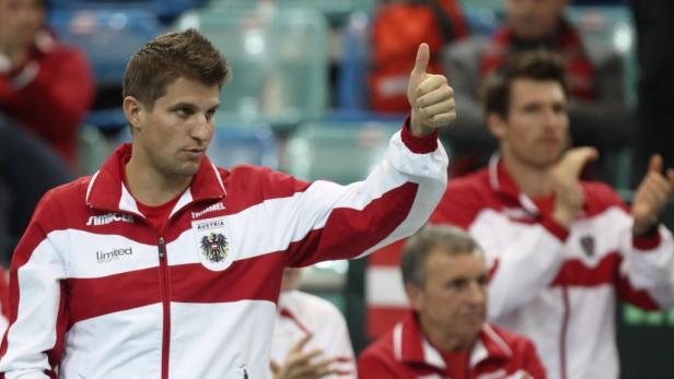 Ein Mann im rot-weißen Trainingsanzug mit österreichischem Wappen zeigt den Daumen nach oben.