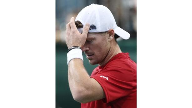 Ein Tennisspieler mit weißer Kappe und rotem Shirt hält sich frustriert den Kopf.