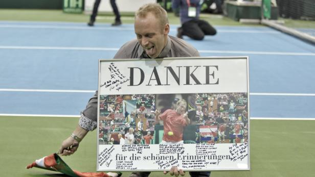 Ein Mann hält ein gerahmtes Poster mit der Aufschrift „Danke“ und Fotos von sich beim Tennisspielen.