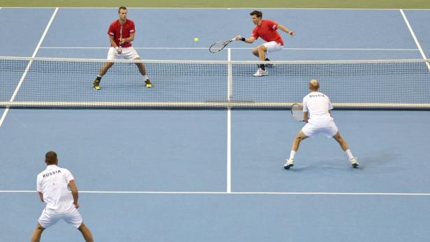 Zwei Doppel-Tennis-Teams spielen auf einem blauen Platz gegeneinander.