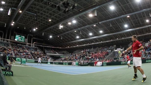 Ein Tennisspieler serviert bei einem Davis-Cup-Spiel in einer Halle.