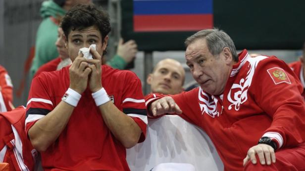 Ein Tennisspieler mit einem Taschentuch im Gesicht, neben ihm sein Trainer mit russischer Flagge im Hintergrund.