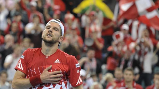 Ein Tennisspieler mit rotem Trikot und weißer Kappe legt die Hand aufs Herz.