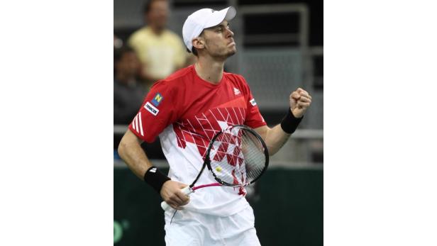 Ein Tennisspieler in rotem Trikot mit geballter Faust auf dem Platz.