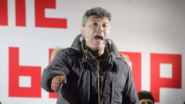 Ein Mann in Winterjacke spricht vor einem Publikum in zwei Mikrofone.