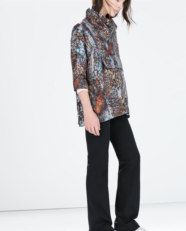 Eine Frau trägt eine gemusterte Jacke und schwarze Hosen.