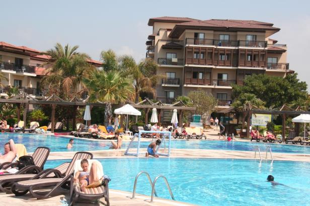 Ein großes Hotel mit Swimmingpool und vielen Menschen, die sich sonnen und schwimmen.