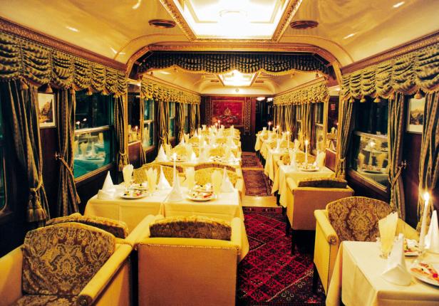 Innenansicht eines luxuriösen Speisewagens mit gedeckten Tischen und Kerzenlicht.