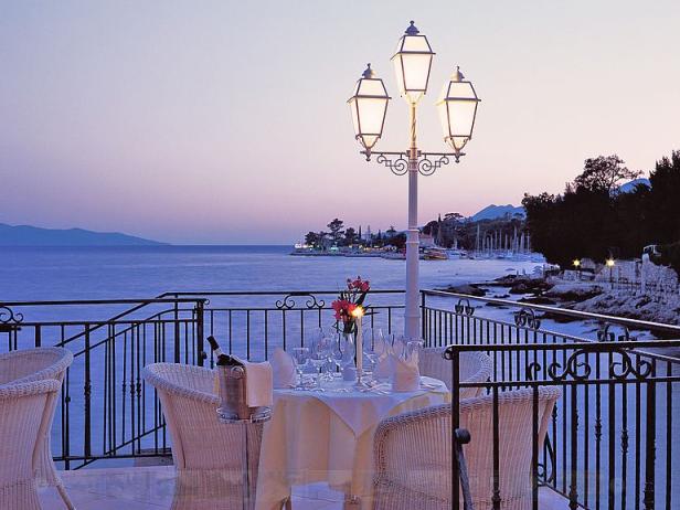 Ein gedeckter Tisch auf einer Terrasse mit Blick auf das Meer bei Dämmerung.