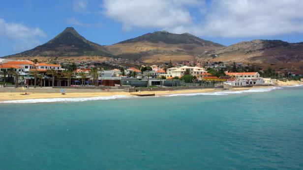 Ein Küstenort mit Strand und Bergen im Hintergrund.