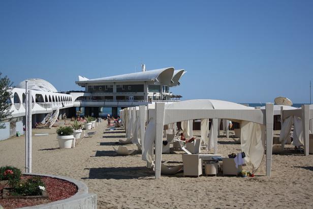 Ein Strand mit weißen Pavillons und einem Gebäude im Hintergrund.