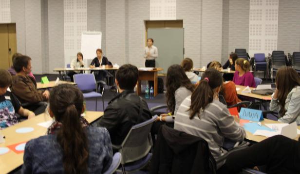 Eine Frau hält einen Vortrag vor einer Gruppe von Menschen in einem Konferenzraum.