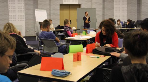 Eine junge Frau hält einen Vortrag vor einer Gruppe von Zuhörern in einem Konferenzraum.