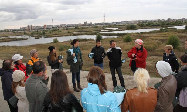 Eine Gruppe von Menschen steht vor einer Seenlandschaft mit einer Stadt im Hintergrund.