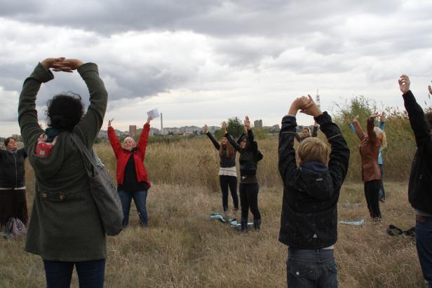 Eine Gruppe von Menschen streckt die Arme in einem Feld unter bewölktem Himmel.