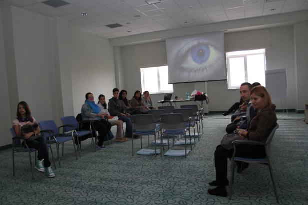 Mehrere Personen sitzen in einem Raum vor einer Leinwand mit dem Bild eines Auges.