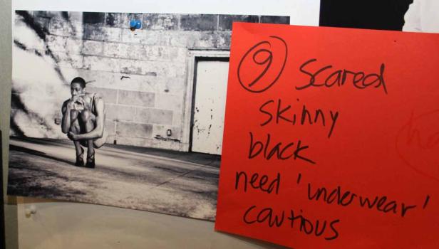 Ein verängstigter, dünner Mann hockt barfuß vor einer Mauer.