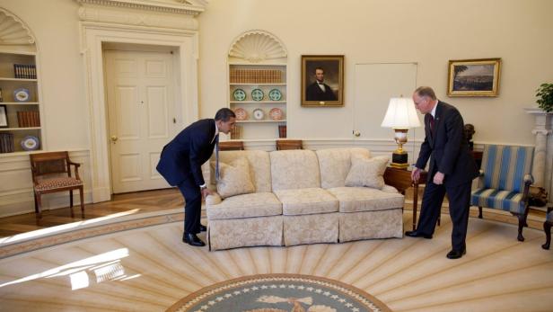 Barack Obama und ein weiterer Mann bewegen ein Sofa im Oval Office.