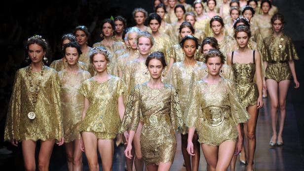 Eine Gruppe von Models in goldfarbenen, römisch inspirierten Outfits auf einem Laufsteg.