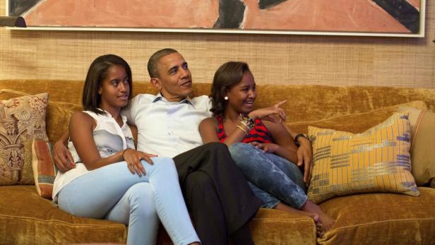 Barack Obama sitzt mit seinen Töchtern Malia und Sasha auf einer Couch.