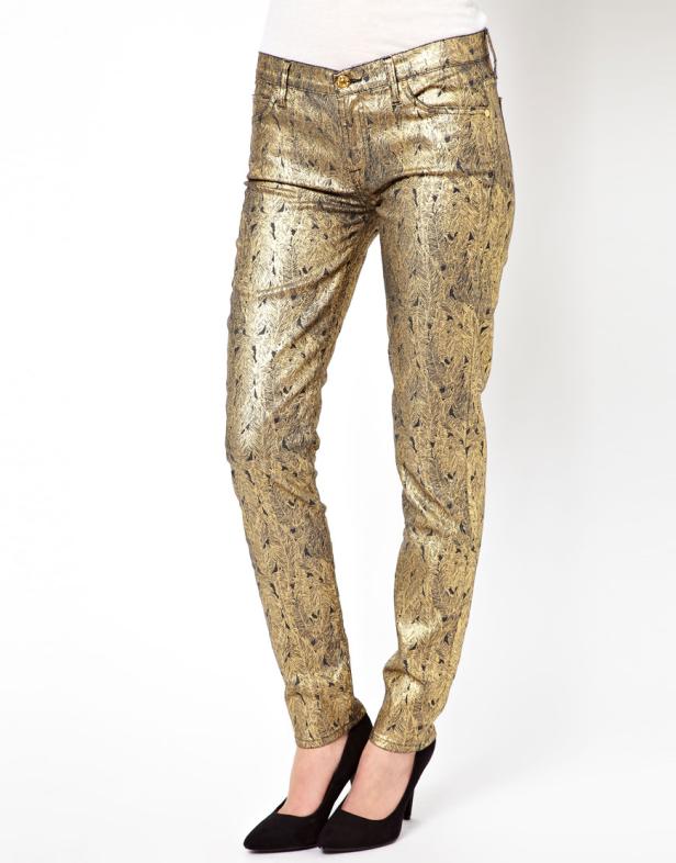 Eine Person trägt goldene, gemusterte Hosen und schwarze High Heels.