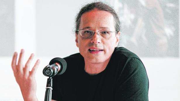 Ein Mann mit Brille gestikuliert vor einem Mikrofon.
