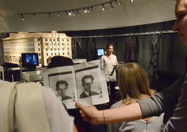 Besucher betrachten in einem Museum ein Modell eines Gebäudes und Porträtfotos.