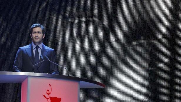Jake Gyllenhaal steht auf einer Bühne vor einer großen Leinwand.