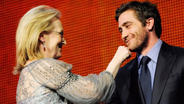 Meryl Streep und Jake Gyllenhaal posieren zusammen vor einem orangefarbenen Hintergrund.