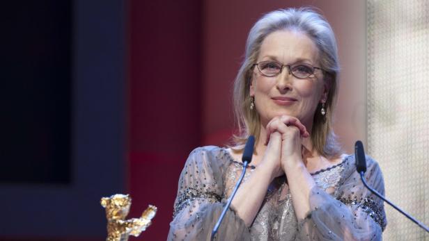 Meryl Streep steht an einem Mikrofon und lächelt.