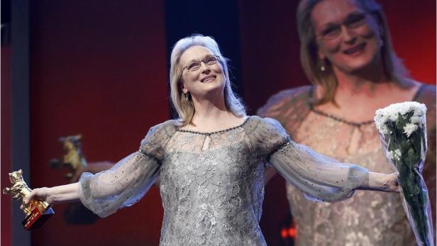 Meryl Streep hält auf einer Bühne einen Goldenen Bären und einen Blumenstrauß.