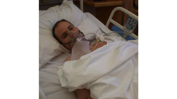 Ein Mann liegt mit einer Atemmaske in einem Krankenhausbett.