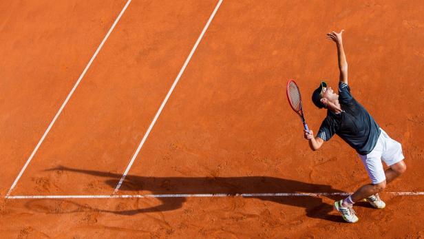 Ein Tennisspieler serviert auf einem Sandplatz.