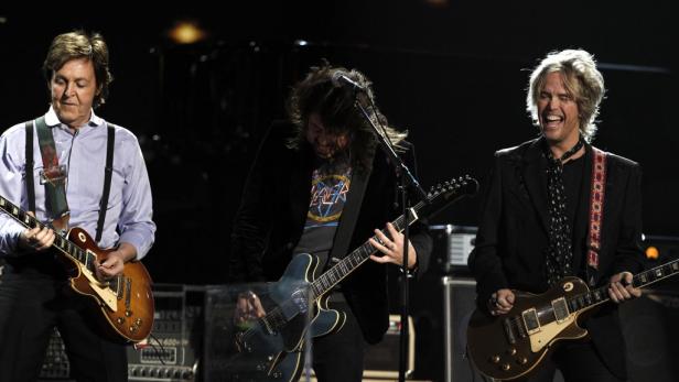 Paul McCartney, Dave Grohl und ein dritter Gitarrist treten gemeinsam auf einer Bühne auf.