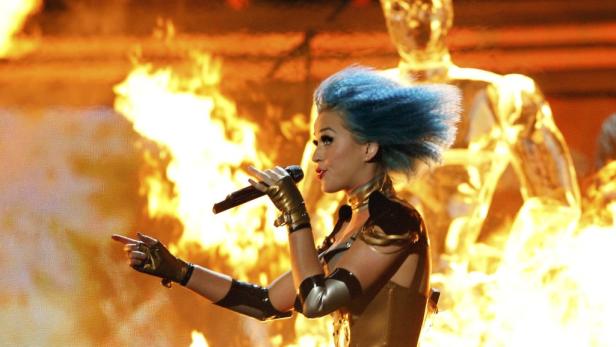 Katy Perry mit blauen Haaren tritt vor einem Hintergrund aus Flammen auf.