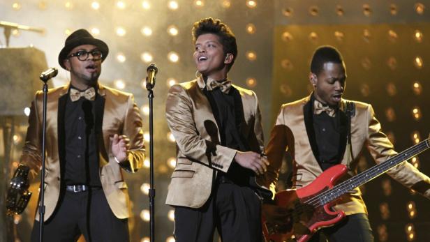Bruno Mars tritt mit seiner Band in goldenen Anzügen auf einer Bühne auf.