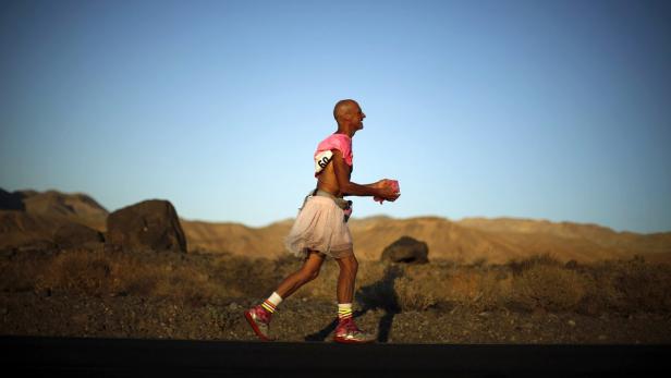 Ein Mann mit einem rosa T-Shirt und einem Tutu läuft durch eine Wüstenlandschaft.