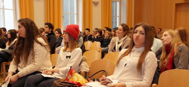 Zahlreiche Menschen sitzen in einem Hörsaal oder Veranstaltungsraum.