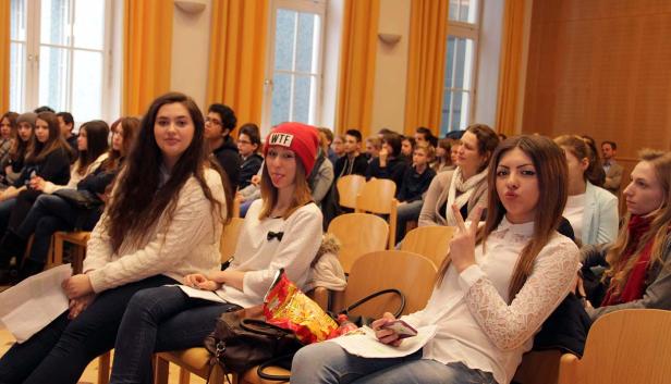 Eine Gruppe junger Leute sitzt in einem Raum und hört aufmerksam zu.