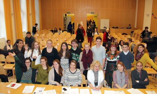 Eine Gruppe von Menschen steht und sitzt in einem großen Raum mit vielen Stühlen.