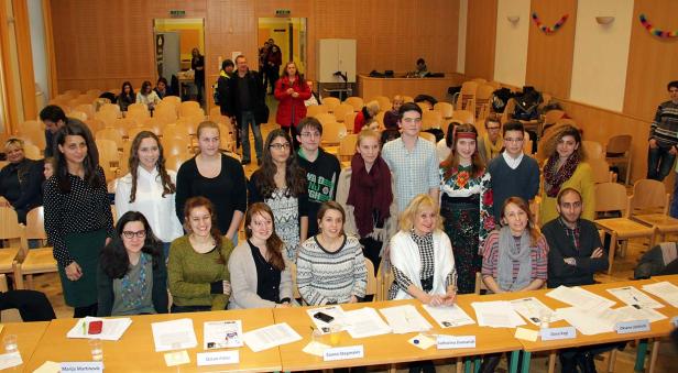 Eine Gruppe von Menschen steht und sitzt hinter Tischen in einem Raum.