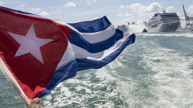 Eine kubanische Flagge weht im Wind, im Hintergrund ein Kreuzfahrtschiff und die Skyline von Miami.
