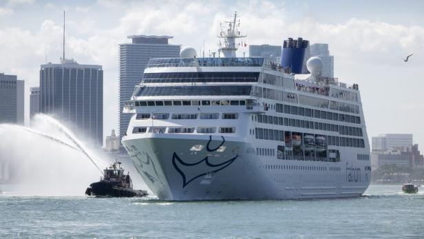 Ein Kreuzfahrtschiff wird von einem Schlepper mit Wasserfontänen auf dem Wasser begleitet.