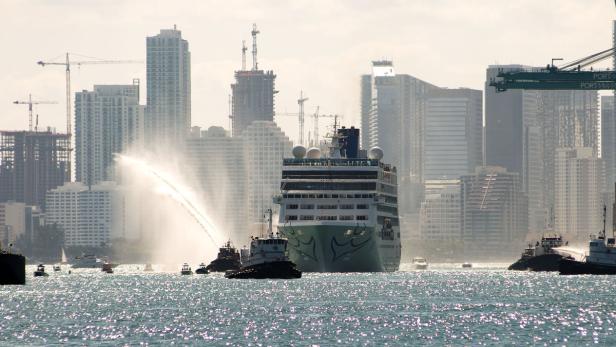 Ein Kreuzfahrtschiff wird im Hafen von Schleppern mit Wasserfontänen begrüßt.