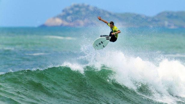 Ein Surfer springt mit seinem Board über eine Welle.