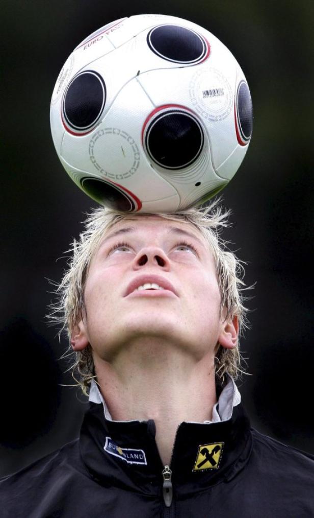 Ein junger Mann balanciert einen Fußball auf seiner Stirn.
