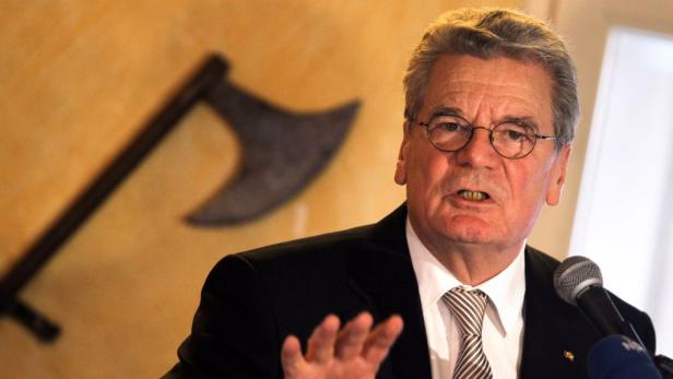 Thomas de Maizière spricht vor einem Mikrofon, im Hintergrund eine Axt an der Wand.
