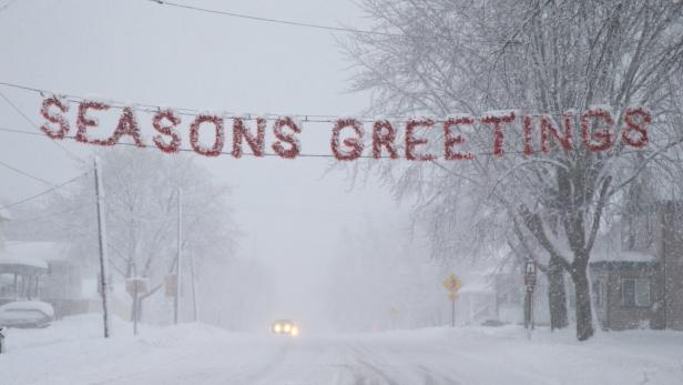 Ein „Seasons Greetings“-Banner überspannt eine verschneite Straße bei starkem Schneefall.