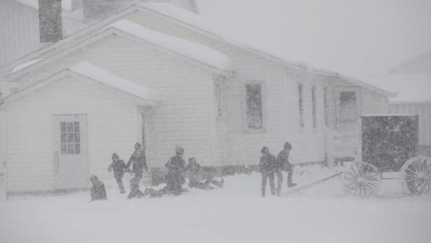Eine Gruppe von Kindern spielt während eines Schneesturms vor einem Haus und einer Kutsche.